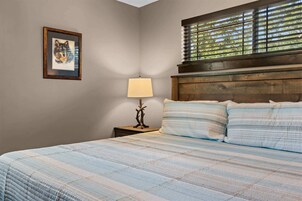 A bedroom with a bed, a nightstand, a lamp, a framed picture, and a window with blinds.