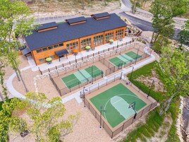 Un edificio de varios pisos con cancha deportiva, asientos al aire libre y estacionamiento.