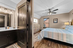 A bedroom with a bed, a ceiling fan, a window with blinds, a dresser, and a bathroom with a mirror and sink. - 8 Tall Oaks - Tall Timbers Escape (Hollister)