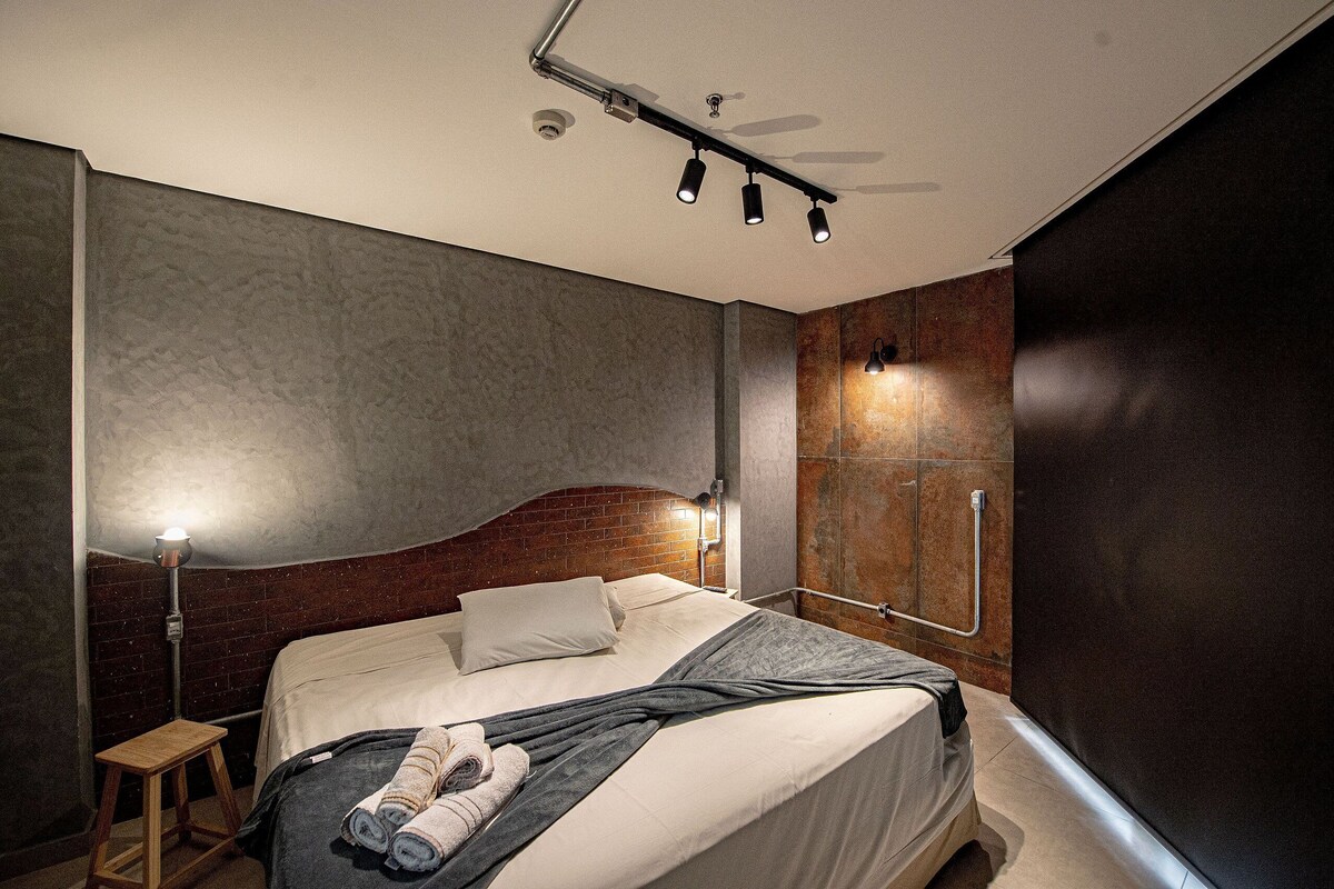 A modern bedroom with a bed, bedside table, and a wall-mounted light fixture.