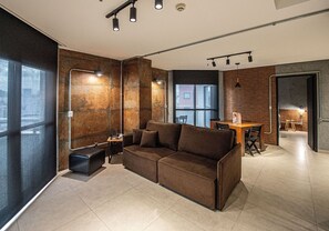 Una sala de estar moderna con un sofá marrón, una mesita y un banco. Hay ventanas amplias y vistas al exterior.