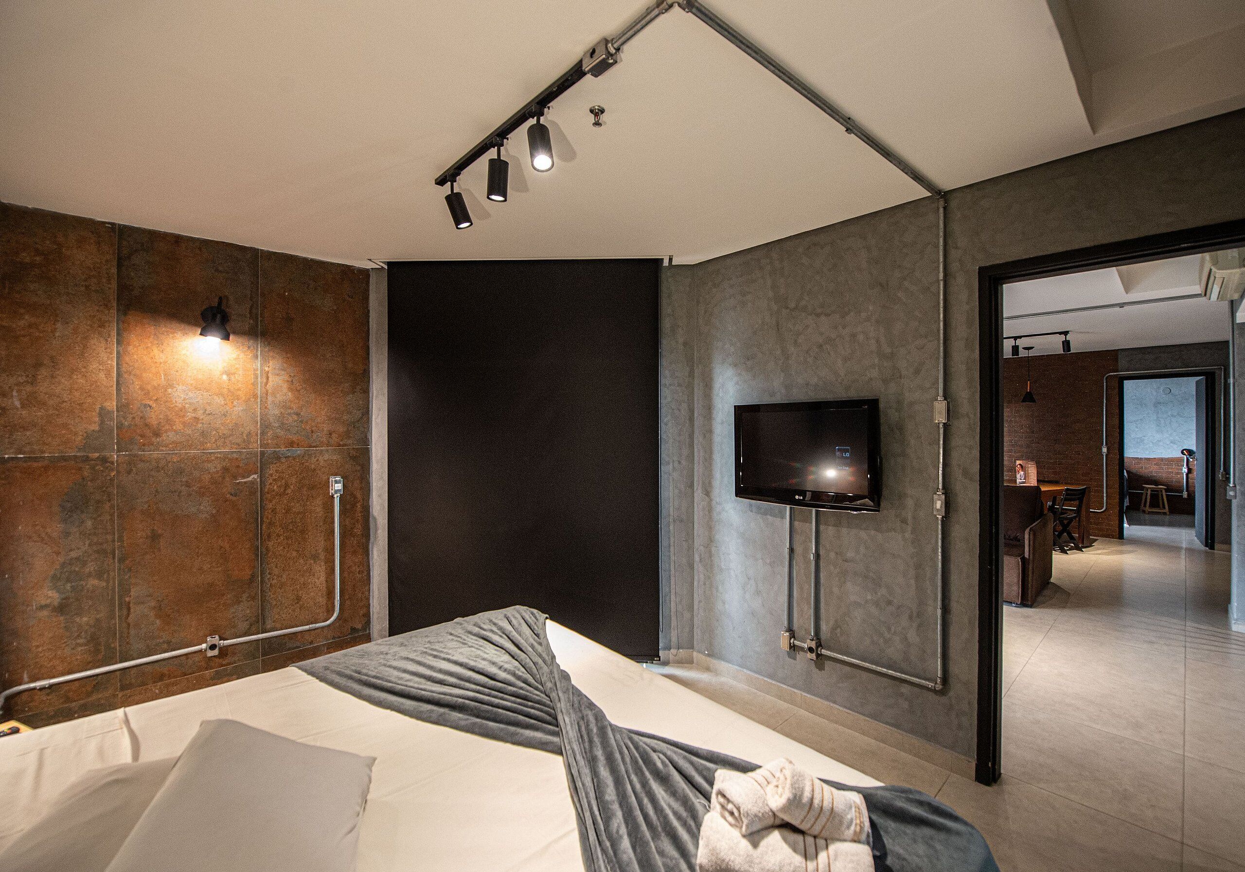 A modern bedroom with a bed, a flat-screen TV mounted on the wall, and a bathroom visible through an open door.