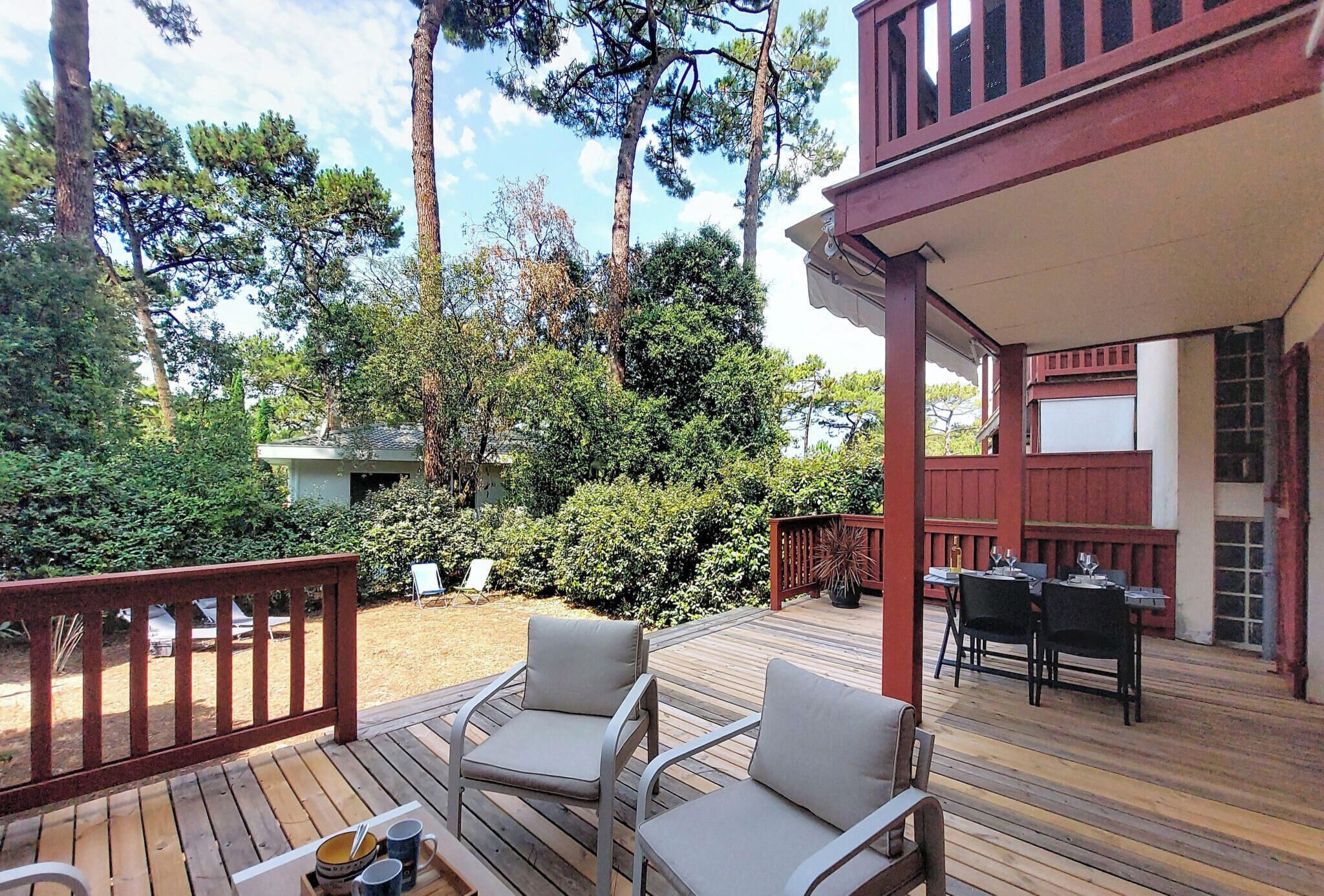 A wooden deck with outdoor furniture, a covered patio area, and a view of a forested area.