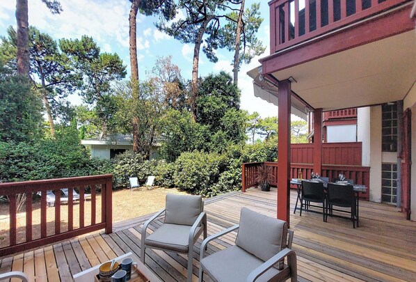 A wooden deck with outdoor furniture, a covered patio area, and a view of a forested area. - Beau Séjour by Interhome (Arcachon)
