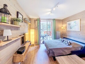 A room with a bed, a desk, a lamp, a shelf with decorative items, and a view through a glass door. - Beau Séjour by Interhome (Arcachon)