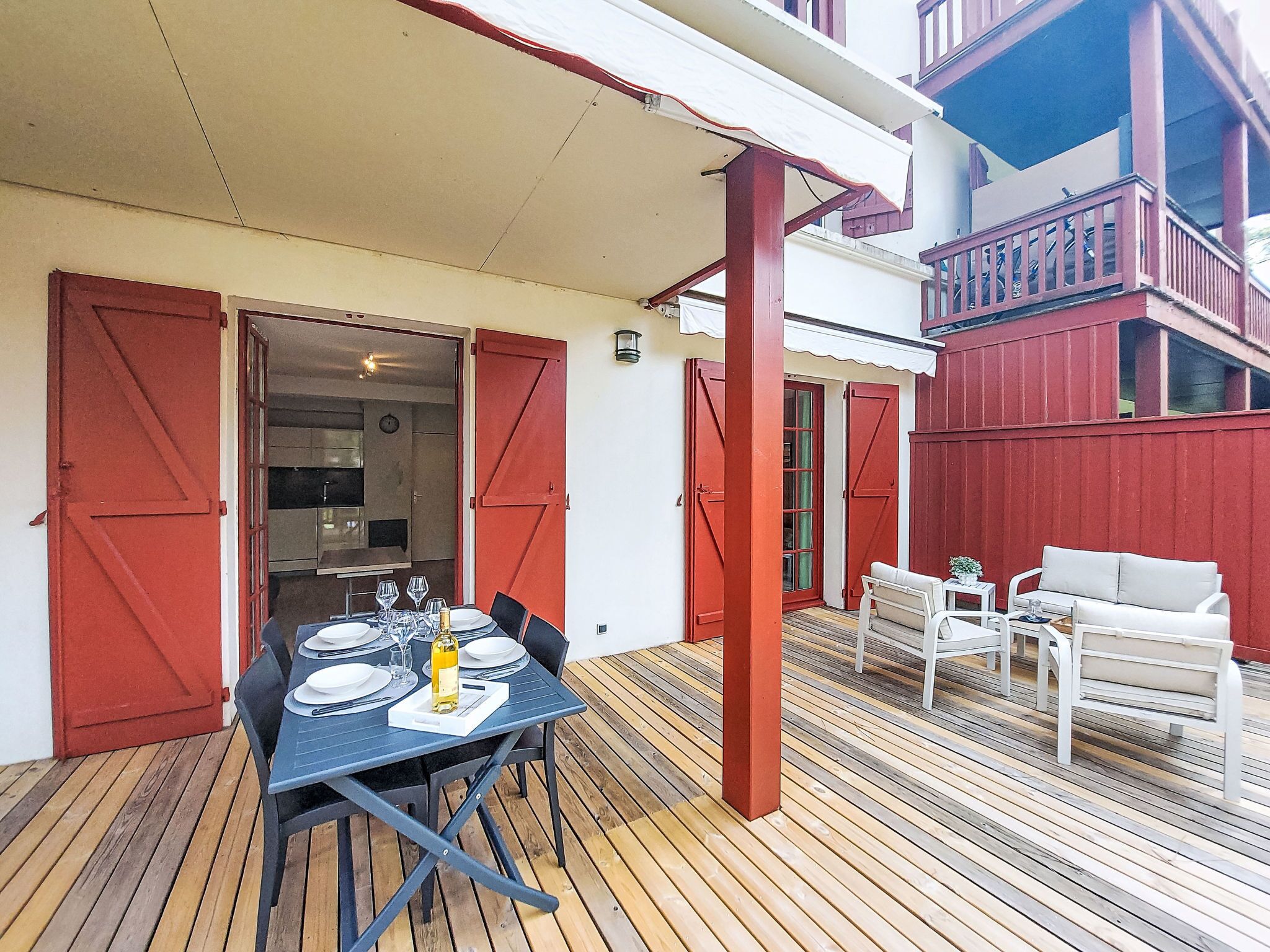 An outdoor dining area with a table set for two, a red door, and a white outdoor bench.