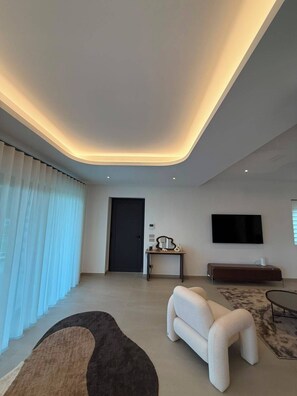 A modern living room with a curved ceiling, a flat-screen TV mounted on the wall, a sofa, a small table with decorative items, and a door. - Casa Magnolia: Spacious Boutique Mountain Home - 4 Bathrooms - Panoramic Views (Sestola)