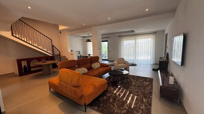 A modern living room with a staircase, a sofa, a coffee table, and a television. - Casa Magnolia: Spacious Boutique Mountain Home - 4 Bathrooms - Panoramic Views (Sestola)