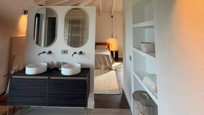 Ein modernes Badezimmer mit einem Doppelwaschtisch, einem großen Spiegel und einer Decke mit freiliegenden Holzbalken.