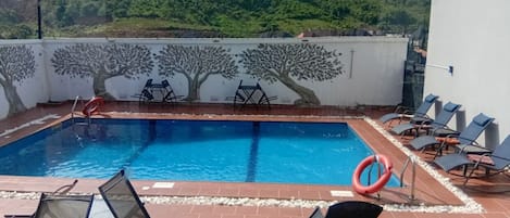A rooftop pool with a view of a hillside, surrounded by lounge chairs and a table.