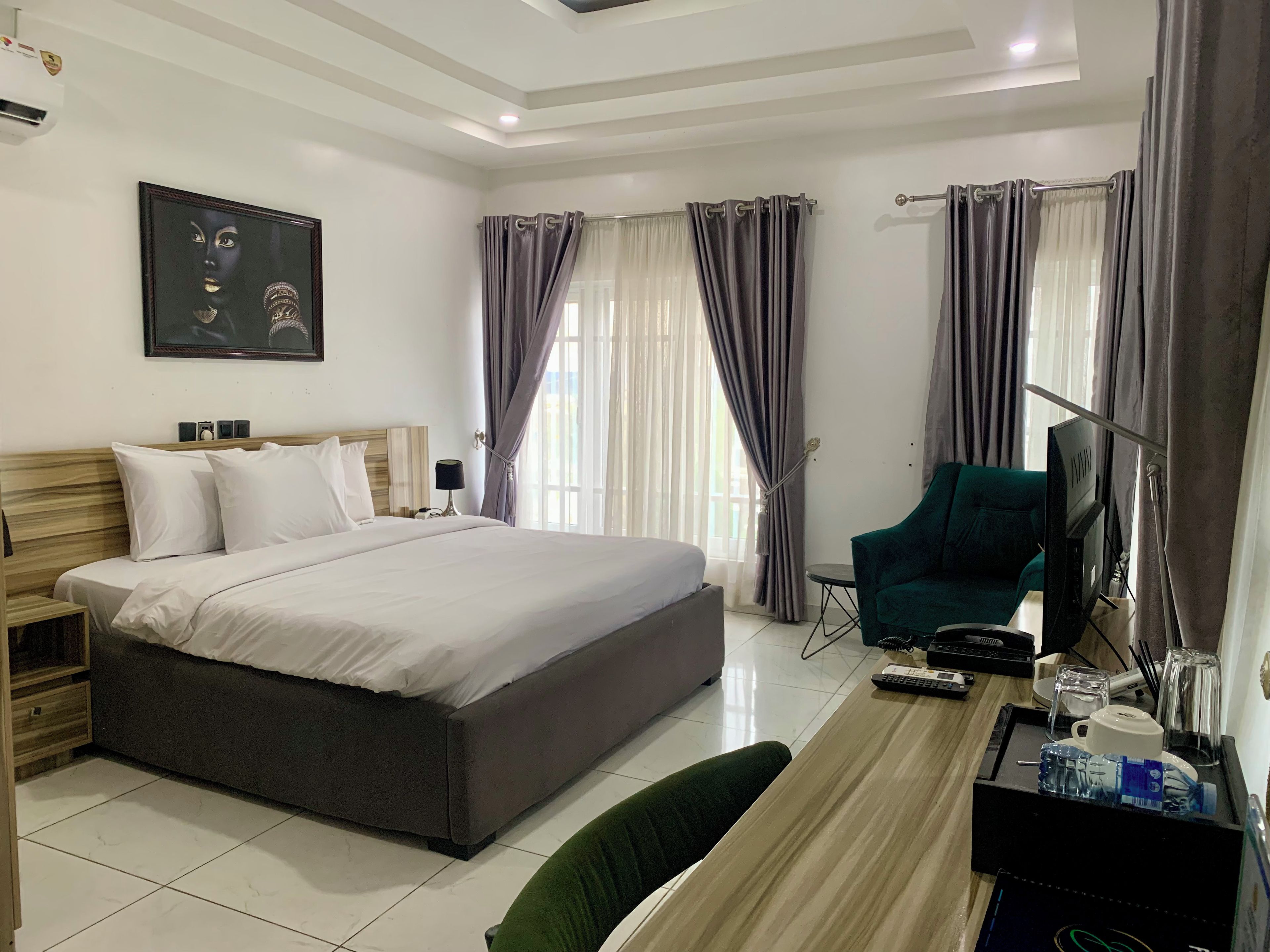 A hotel room with a large bed, a desk with a chair, a television, and a painting on the wall.