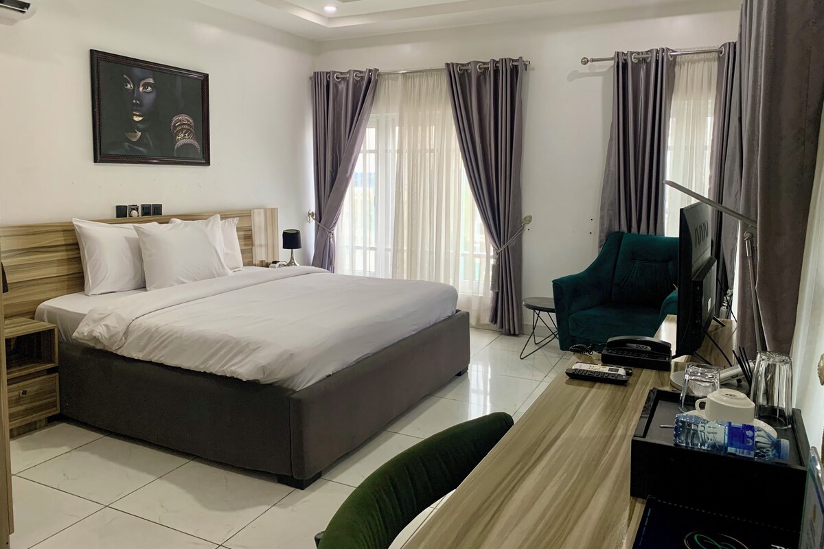 A hotel room with a large bed, a desk with a chair, a television, and a painting on the wall.