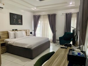 A hotel room with a large bed, a desk with a chair, a television, and a painting on the wall. - Devon's Villa and Apartments Apo (Abuja)
