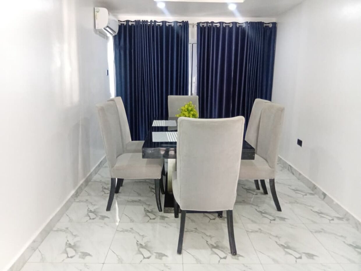 A dining area with a table and four chairs, a small plant on the table, and a window with curtains.