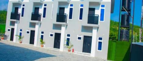 A modern multi-story building with balconies, a paved driveway, and potted plants.
