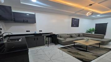 A modern living room with a sofa, a coffee table, and a kitchen area with cabinets and a sink.