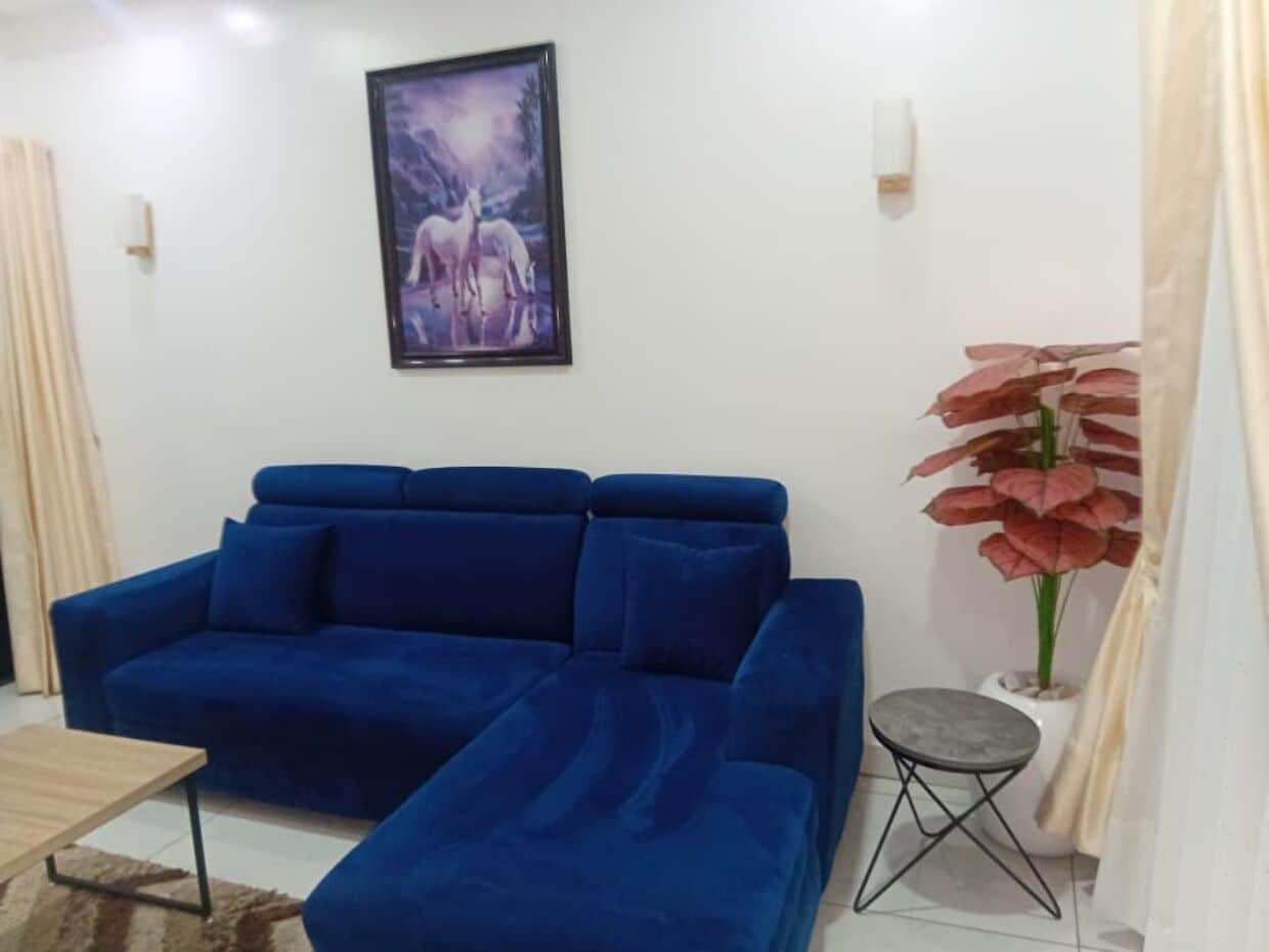A room with a blue sofa, a small table, a framed picture on the wall, and a potted plant.