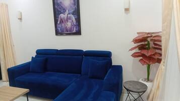 A room with a blue sofa, a small table, a framed picture on the wall, and a potted plant.