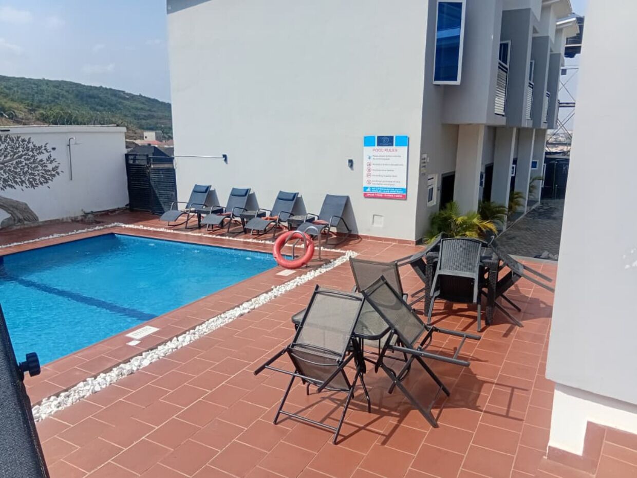 Un área de piscina en la azotea con sillas de descanso y un cartel que indica las normas de la piscina.