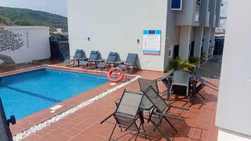 Un área de piscina en la azotea con sillas de descanso y un cartel que indica las normas de la piscina.