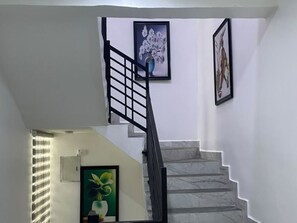 A staircase with a black handrail and white walls, leading to an upper floor. - Devon's Villa and Apartments Apo (Abuja)