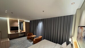A hotel room with a large bed, a desk with a flat-screen TV, a seating area with chairs, and a large window with curtains. - NEWLEVEL HOTEL (MAKKAH)