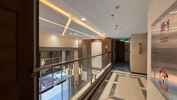 A modern hotel corridor with glass railings, a ceiling with recessed lighting, and a fire hose reel sign. - NEWLEVEL HOTEL (MAKKAH)