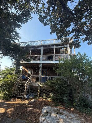 A two-story wooden cabin with a balcony, surrounded by trees. - Spacious 5-bedroom house in fantastic Ocracoke with AC (Ocracoke)