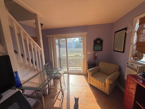 A room with a glass table, a cushioned armchair, a red cabinet, and a window with blinds. - Spacious 5-bedroom house in fantastic Ocracoke with AC (Ocracoke)