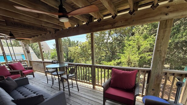 A covered deck with a table and chairs, a sofa, and a pool in the background.