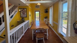 A dining area with a long wooden table, white railings, and a view through a window.