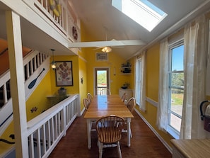 A dining area with a long wooden table, white railings, and a view through a window. - Spacious 5-bedroom house in fantastic Ocracoke with AC (Ocracoke)