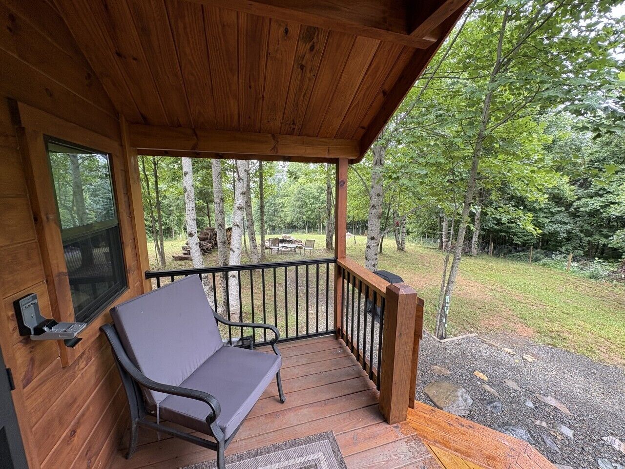 Une terrasse en bois avec un banc, une fenêtre et une vue sur une zone boisée.