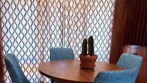 A round wooden table with a terracotta pot containing two cacti, surrounded by four blue upholstered chairs with metal legs.