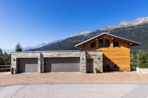 A modern building with two garage doors, a wooden exterior, and a mountain backdrop. - Villa moderne avec Jacuzzi - ski - golf (Icogne)