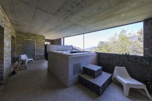A modern kitchen with a large island, a view of the outdoors, and a stone wall. - Villa moderne avec Jacuzzi - ski - golf (Icogne)