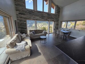 A spacious living area with a stone wall, a sofa set, a round coffee table, and a dining table with chairs. - Villa moderne avec Jacuzzi - ski - golf (Icogne)