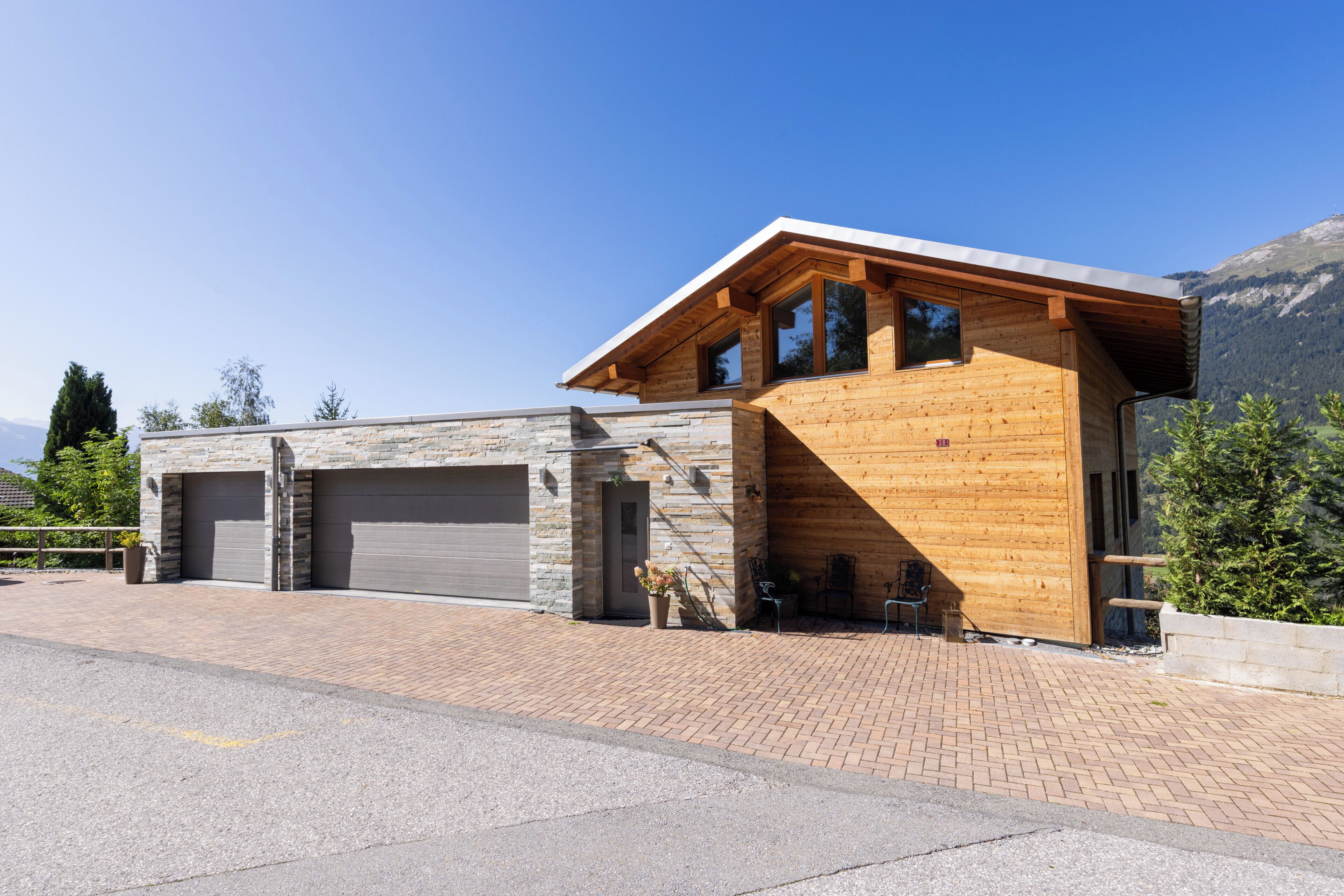 Een modern gebouw met een stenen gevel en houten bovenverdiepingen, met een garage en een terras.