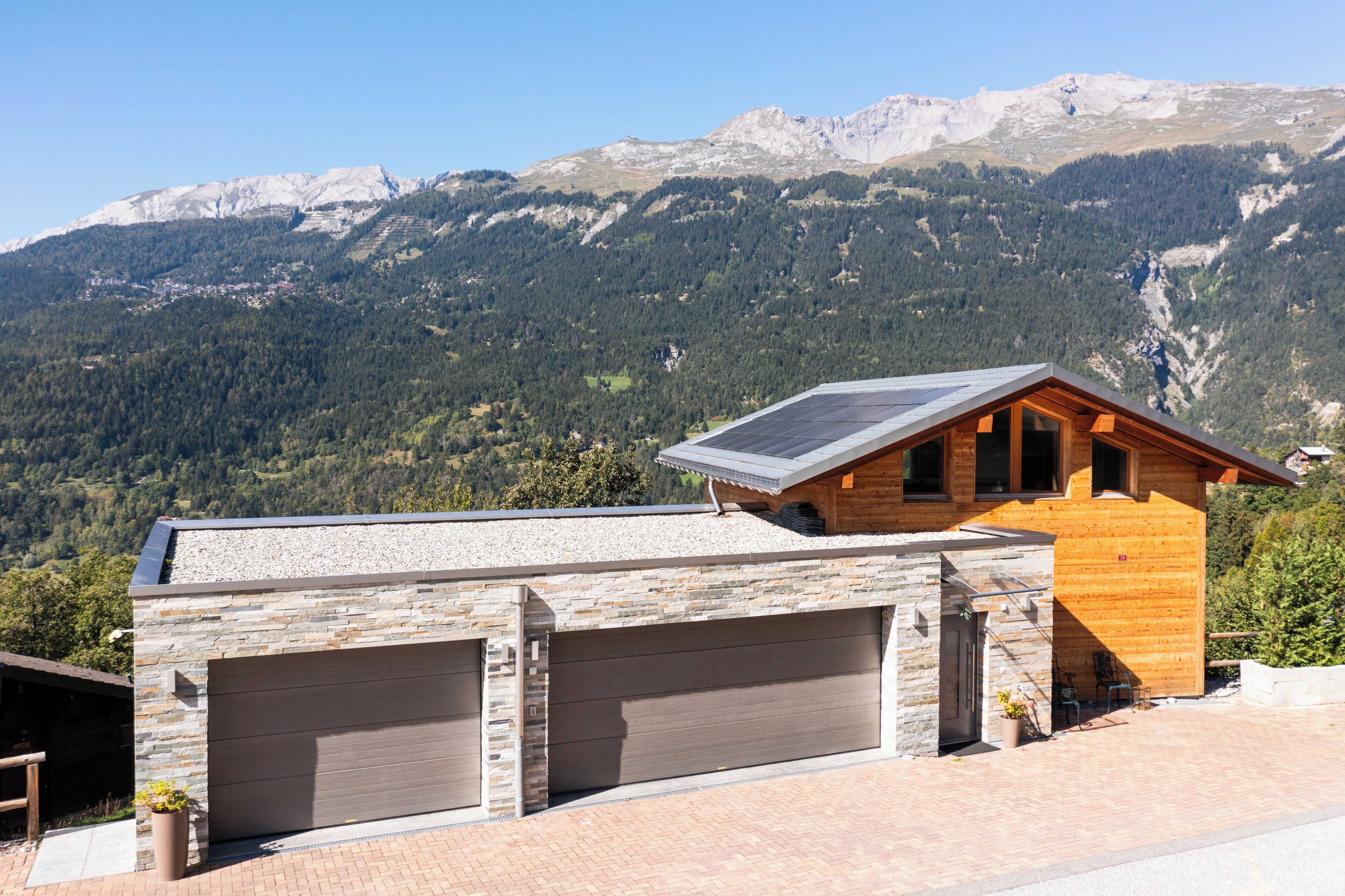 A modern building with a garage, stone facade, and a wooden structure with a sloped roof.