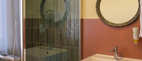 Un baño moderno con ducha de vidrio, lavabo blanco y tocador de madera con toallas.