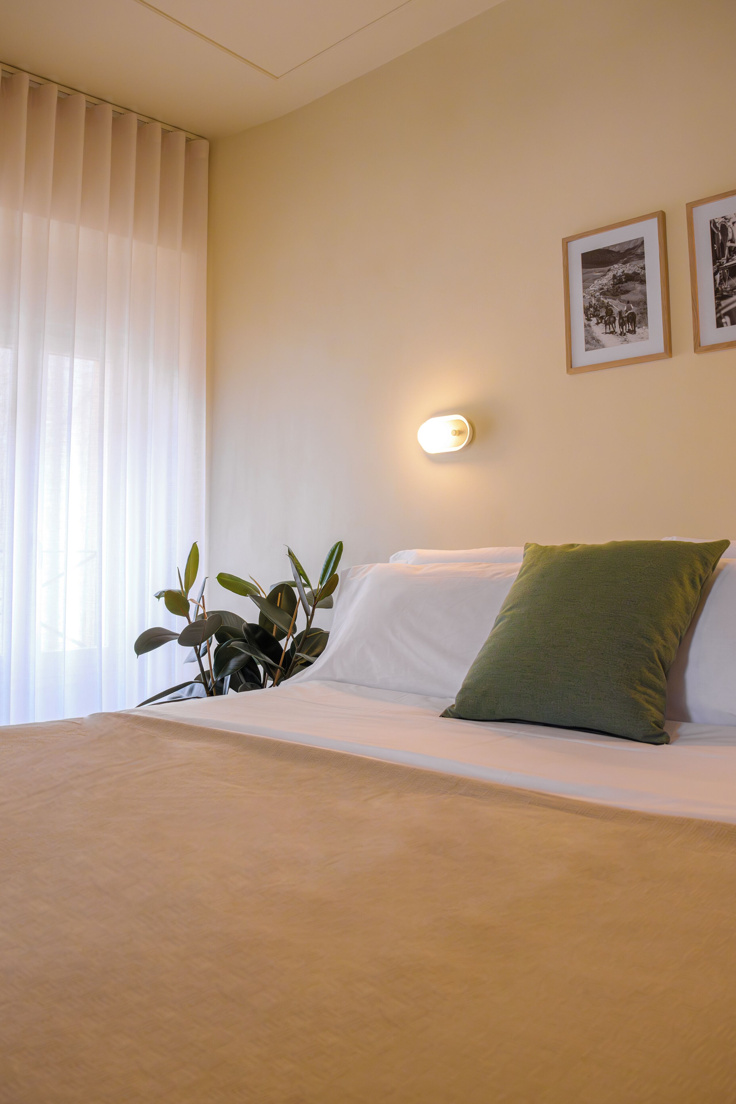 Ein Hotelzimmer mit einem Bett, einem grünen Kopfkissen, einer Wandleuchte und zwei gerahmten Bildern.