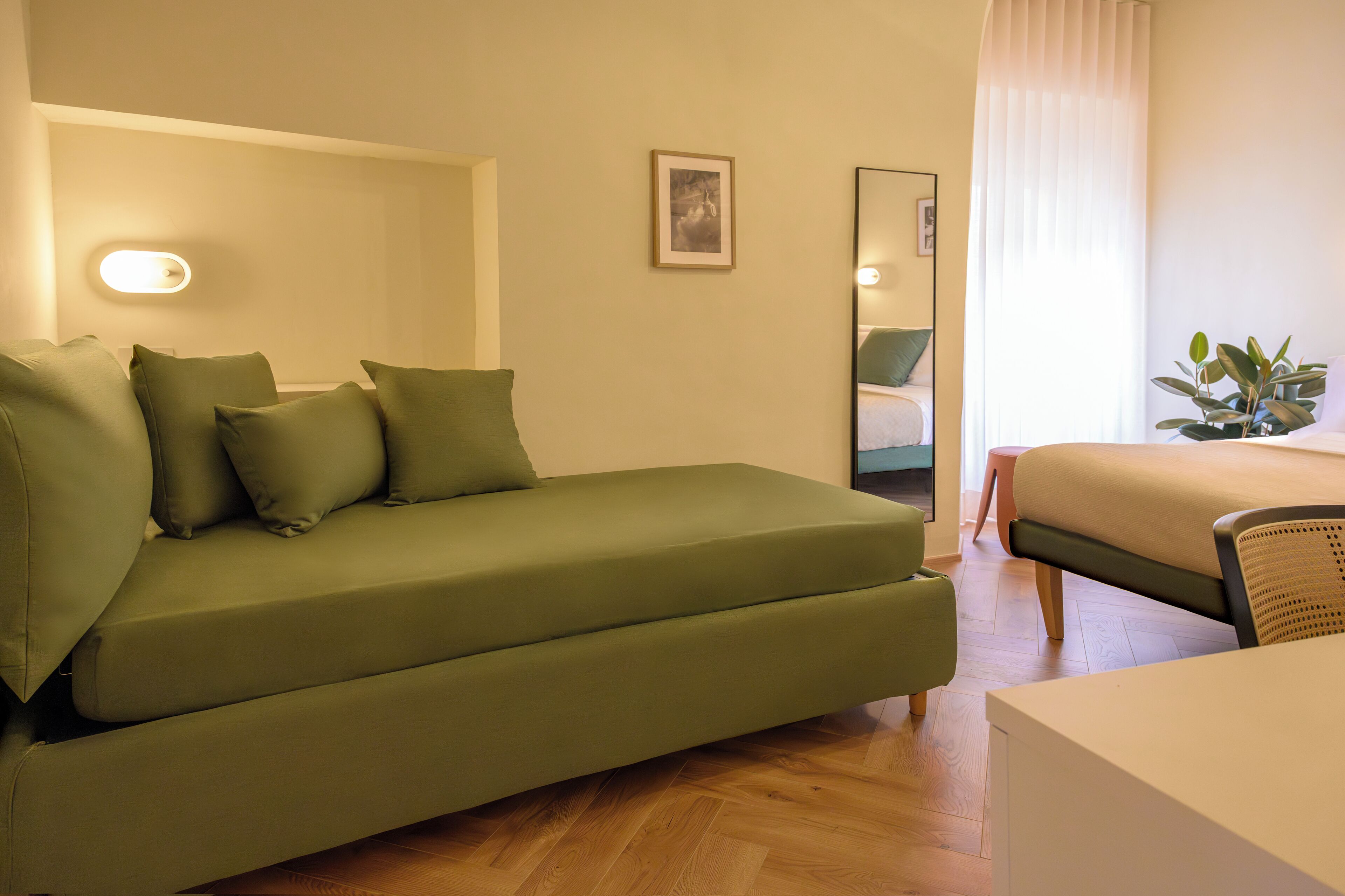 Une pièce avec un canapé vert, un lit, une petite table et un miroir.