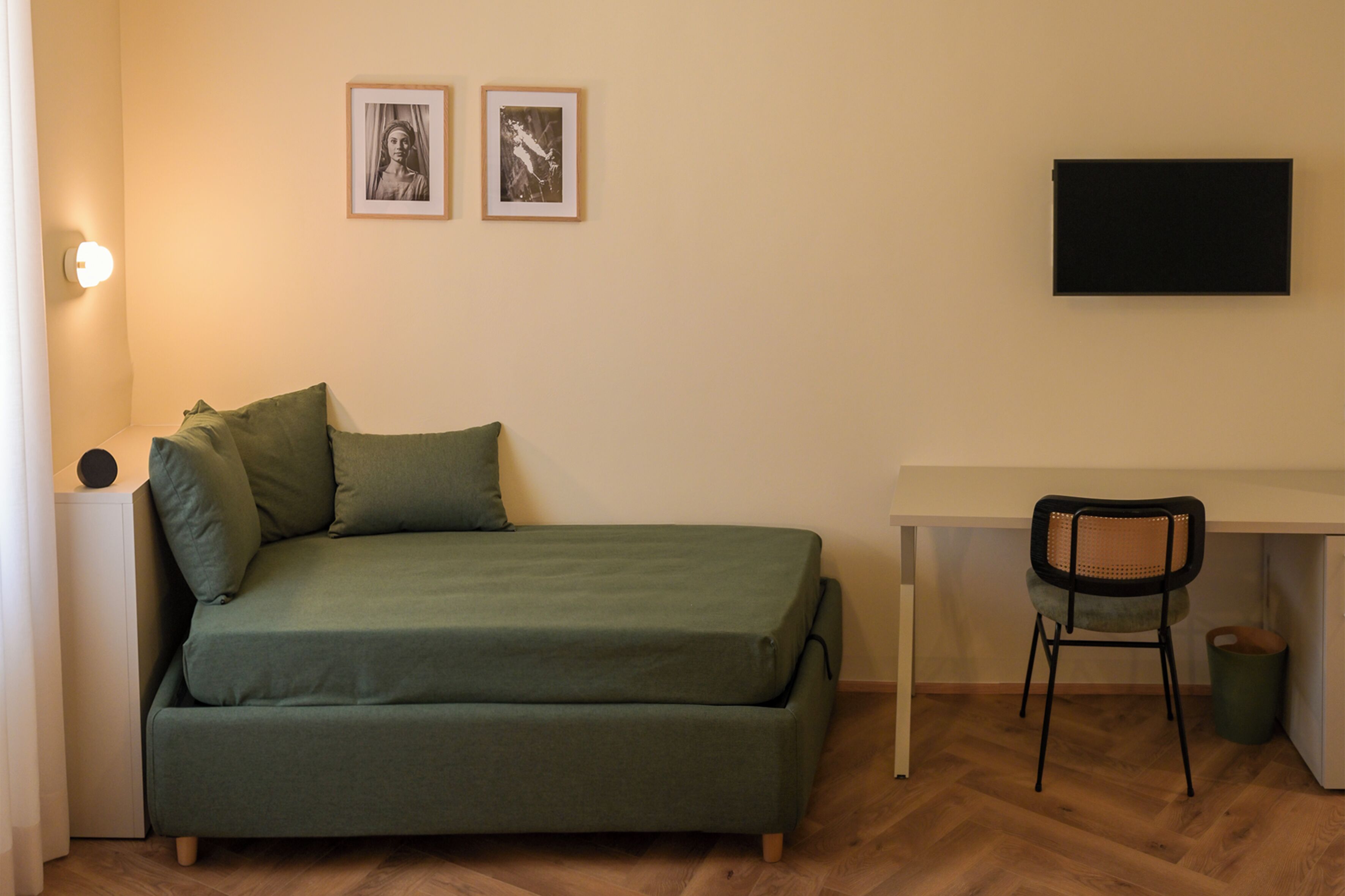 A room with a green sofa, a desk, a chair, and two framed pictures on the wall.