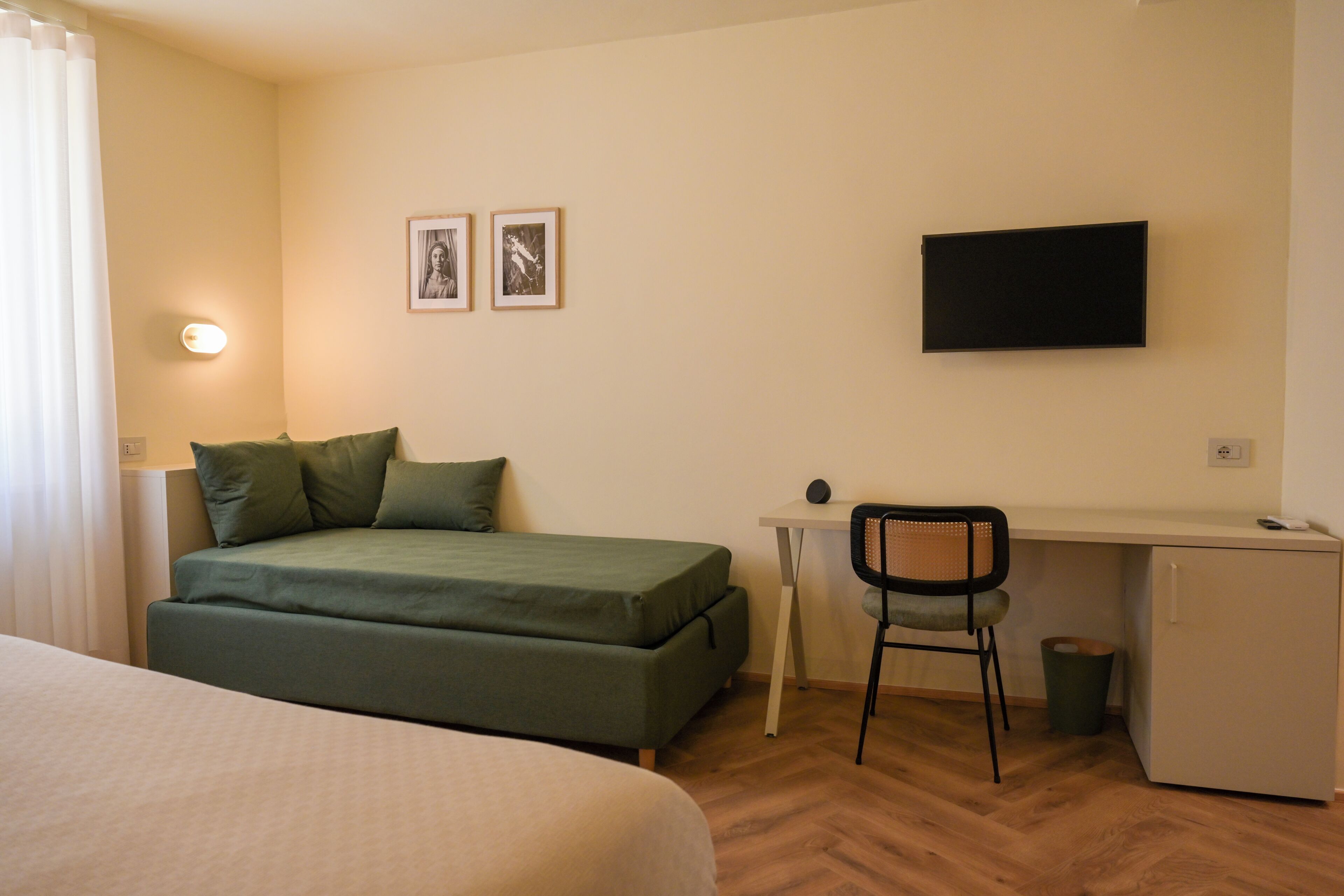 Una habitación con cama, escritorio, silla, televisor y dos cuadros en la pared.