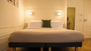 Un lit bien fait, avec un oreiller vert et du linge de lit blanc, des pieds en bois et une tête de lit agrémentée de lampes fixées au mur.