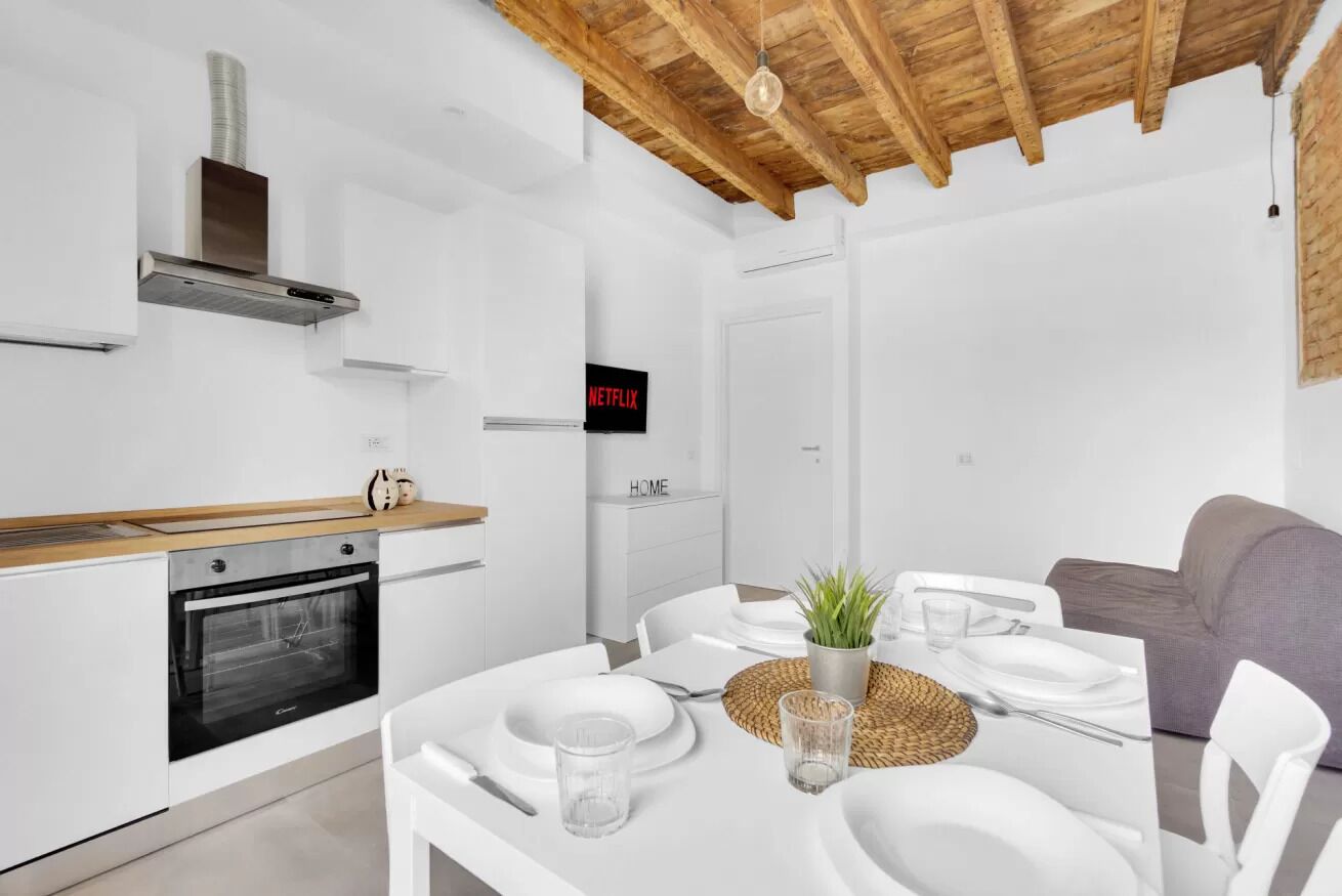 Una cucina moderna con mobili bianchi, forno integrato e soffitto in legno.