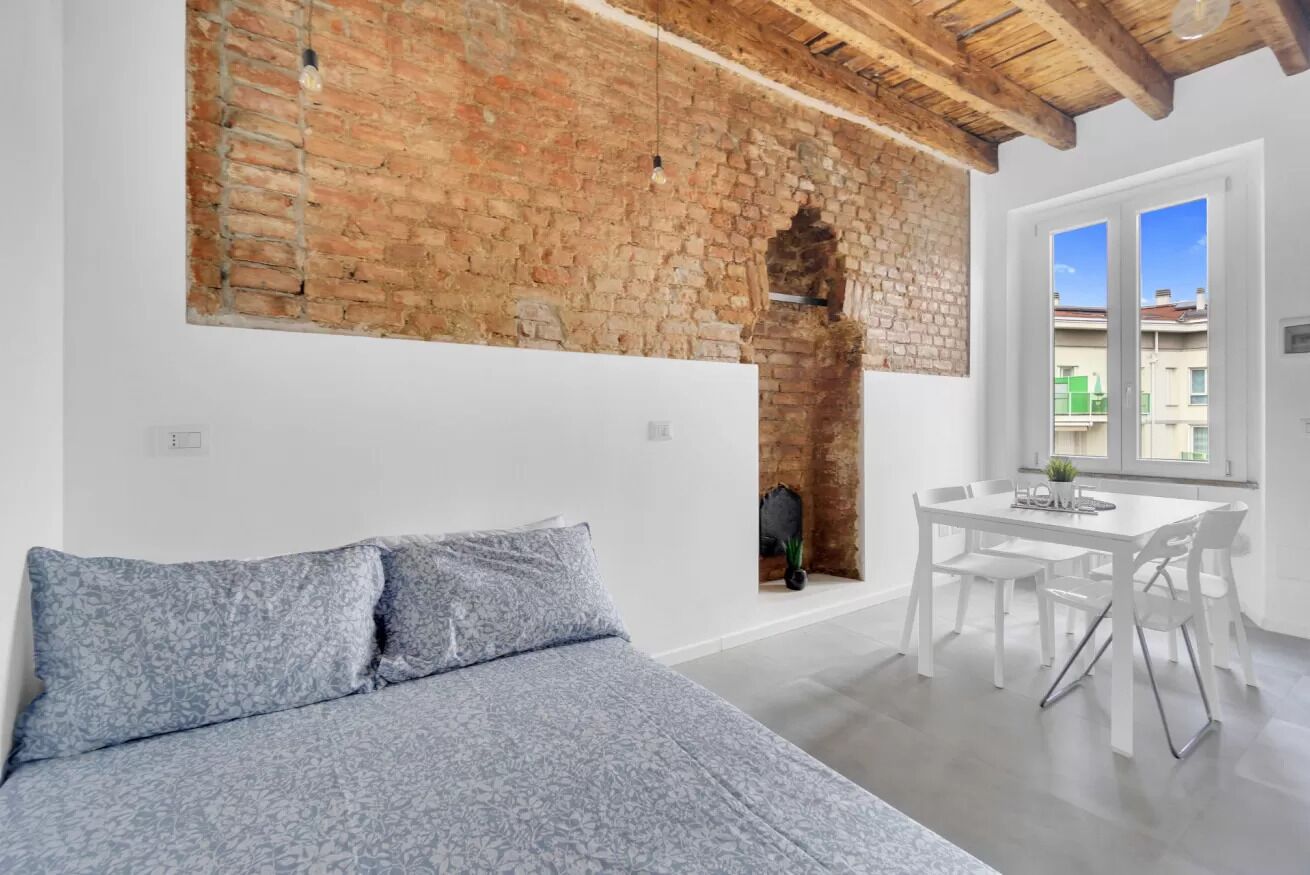Una camera da letto con un letto, un tavolo da pranzo con sedie, una parete in mattoni e una finestra.