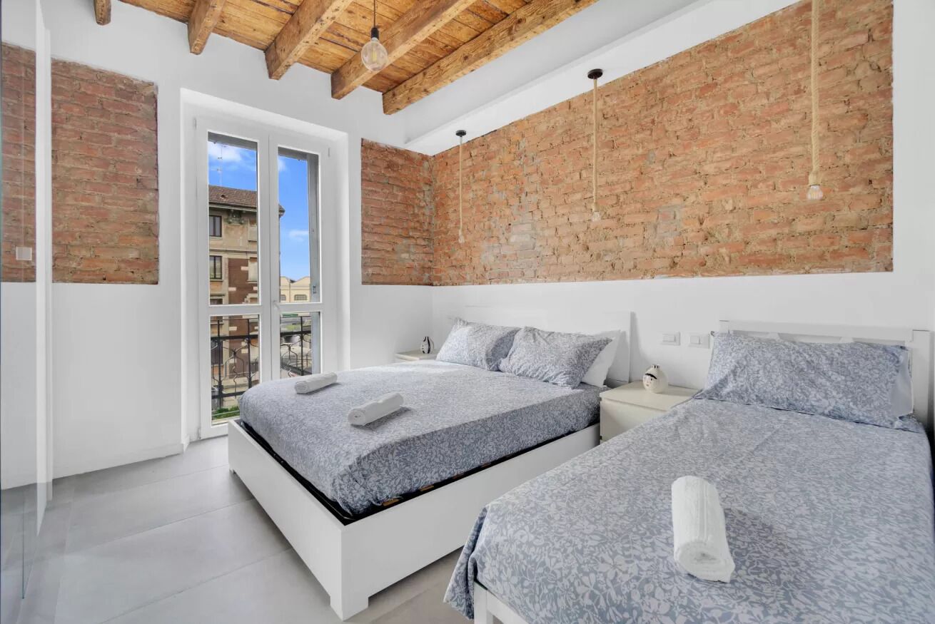 A modern bedroom with two beds, a brick wall, and a balcony.