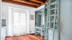 Ein Zimmer mit Holzboden, einem Schreibtisch mit Stuhl, einem Bücherregal und einem Fenster mit weißem Vorhang.