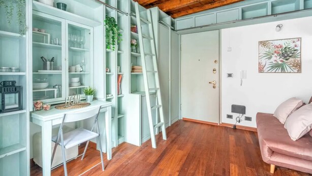 Ein Zimmer mit weißem Schreibtisch, einem rosafarbenen Sofa, einem weißen Schrank mit Glastüren und einer Holzbodenverkleidung.